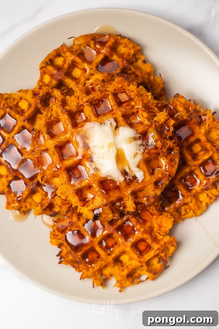 A stack of golden-brown Sweet Potato Waffles, perfectly cooked and generously topped with a pat of melting butter, presented invitingly on a white plate.