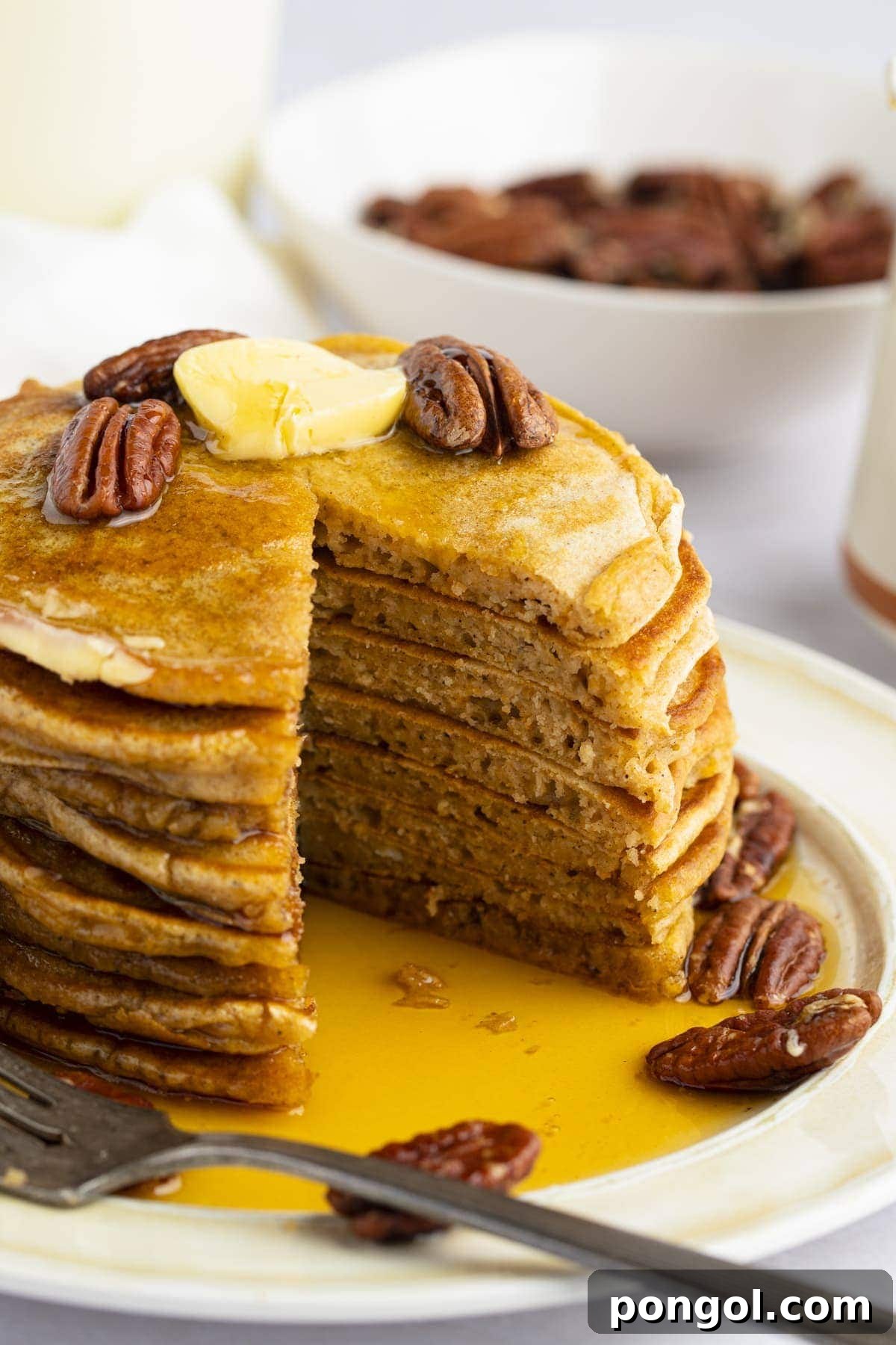 A beautifully stacked tower of fluffy sweet potato pancakes, generously topped with roasted pecans and a pat of melting butter, with a delicious triangular wedge already cut out and resting on a fork.