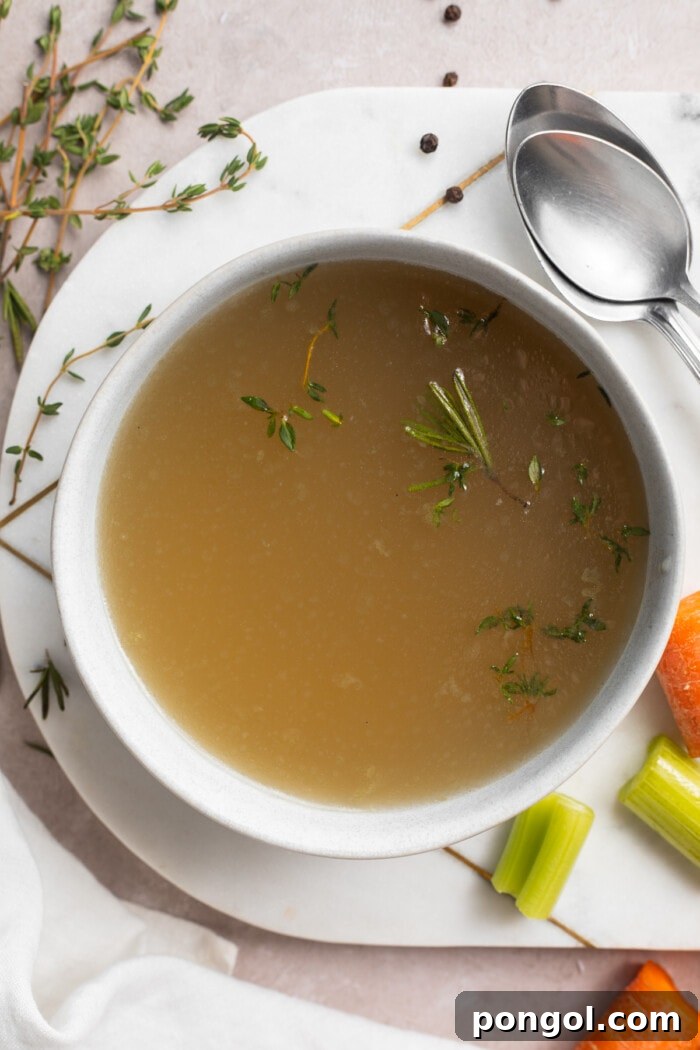 An overhead shot of a rustic bowl of stovetop bone broth, garnished with vibrant fresh herbs, artfully arranged on an oval platter to highlight its homemade goodness and appealing presentation.