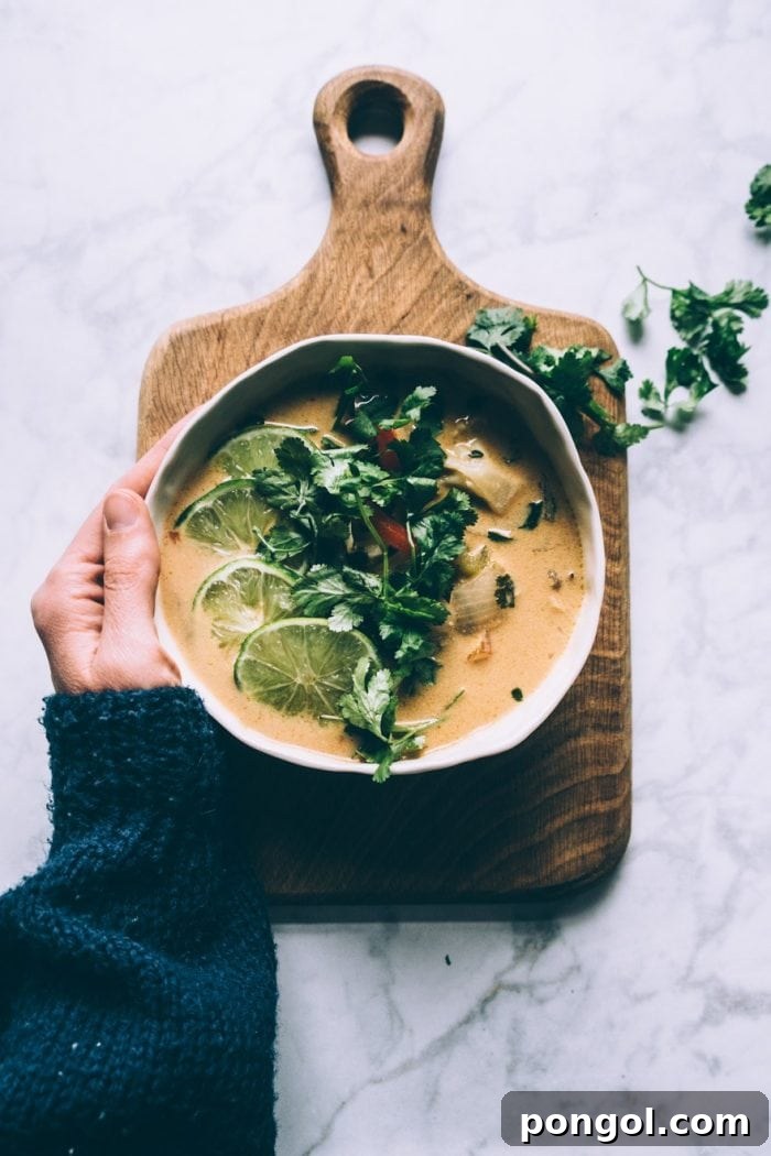 A bowl of creamy Thai Coconut Cauliflower Soup, garnished with fresh cilantro and a slice of lime, highlighting its rich texture.