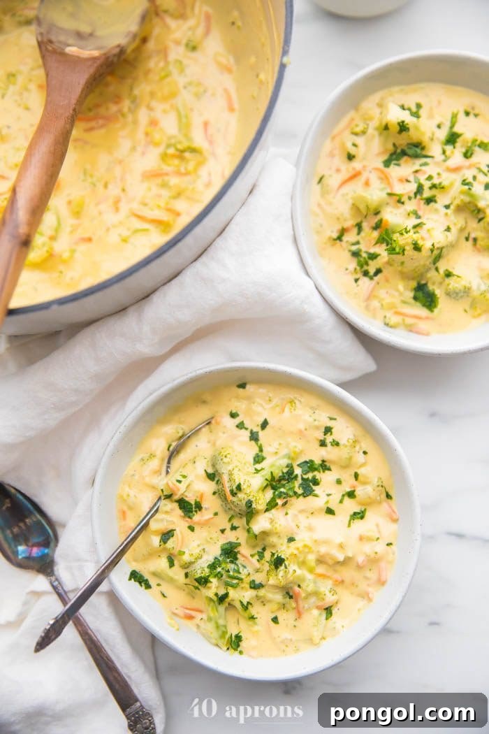Two bowls of creamy, rich Cheesy Vegan Broccoli Soup, topped with fresh herbs, showcasing its vibrant green color.