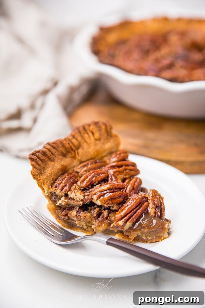 A slice of paleo pecan pie artfully arranged on a white plate with a silver fork, highlighting its rich texture and inviting warmth.