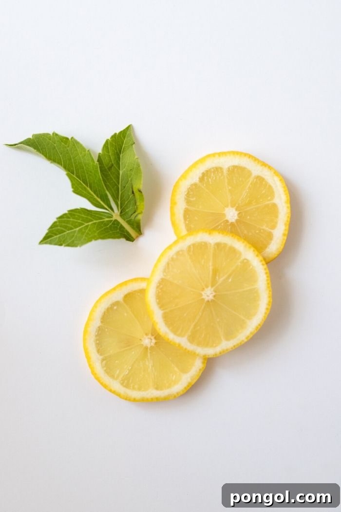 Three bright slices of fresh lemon and vibrant mint leaves are artfully arranged against a clean white background, symbolizing natural cleansing and refreshment.