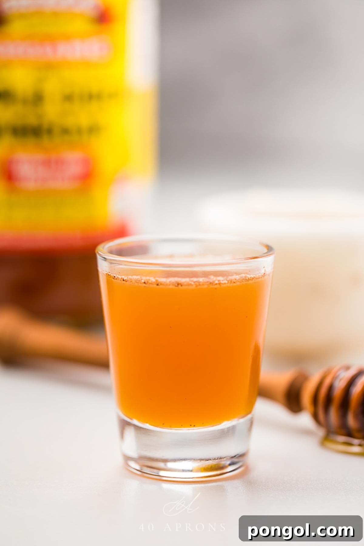 A clear glass shotglass holding an orange liquid peppered with cinnamon, ready to be consumed as an Apple Cider Vinegar Honey Shot.