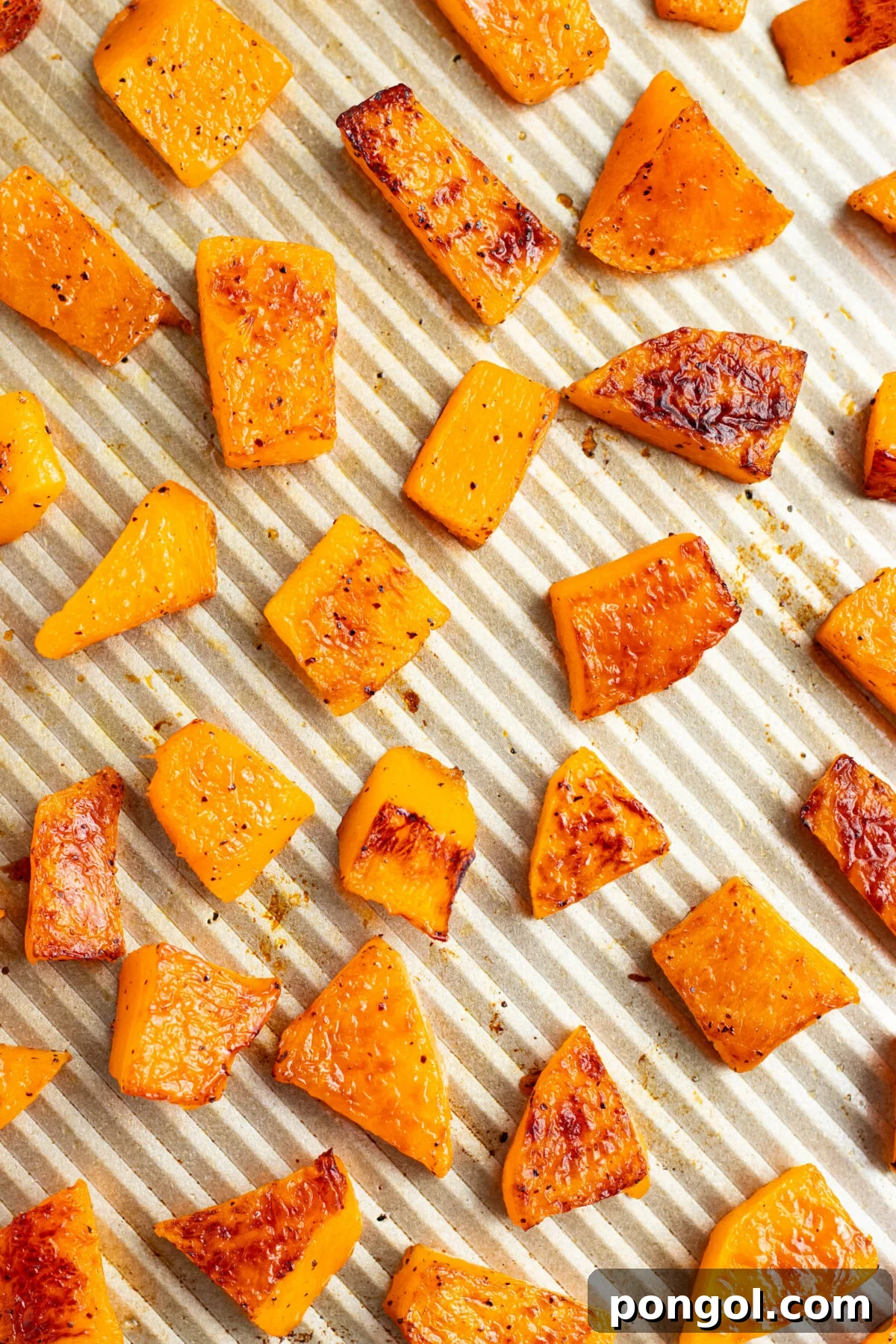 Cubed, oven-roasted butternut squash on a silver baking sheet.