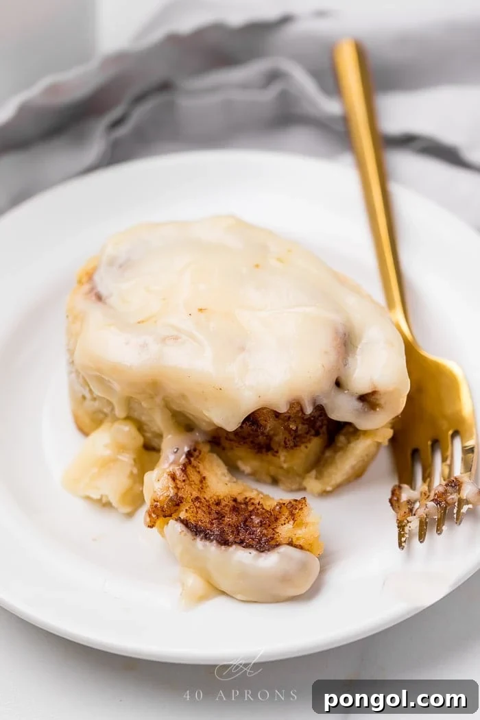 A perfectly baked gluten-free cinnamon roll drizzled with cream cheese frosting, served on a white plate with a fork, ready to be enjoyed.