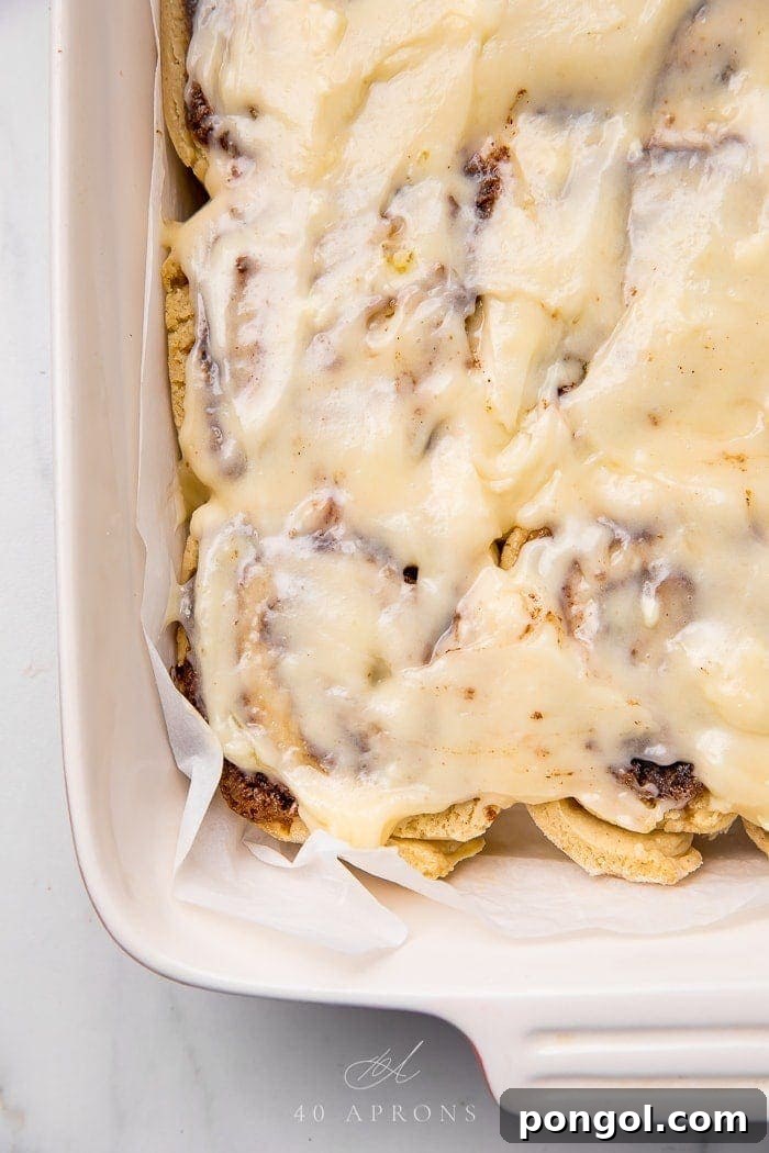 A baking pan filled with freshly baked gluten-free cinnamon rolls generously topped with rich cream cheese frosting.