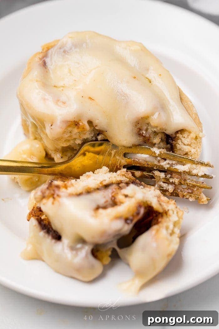 A freshly baked gluten-free cinnamon roll cut in half, revealing its perfectly swirled cinnamon filling and soft texture, with a fork beside it.
