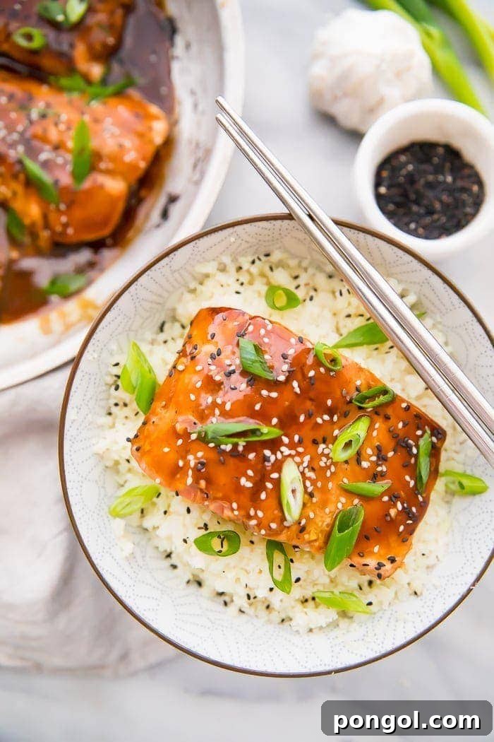 Teriyaki salmon served in a bowl with cauliflower rice and chopsticks, garnished with green onions and sesame seeds