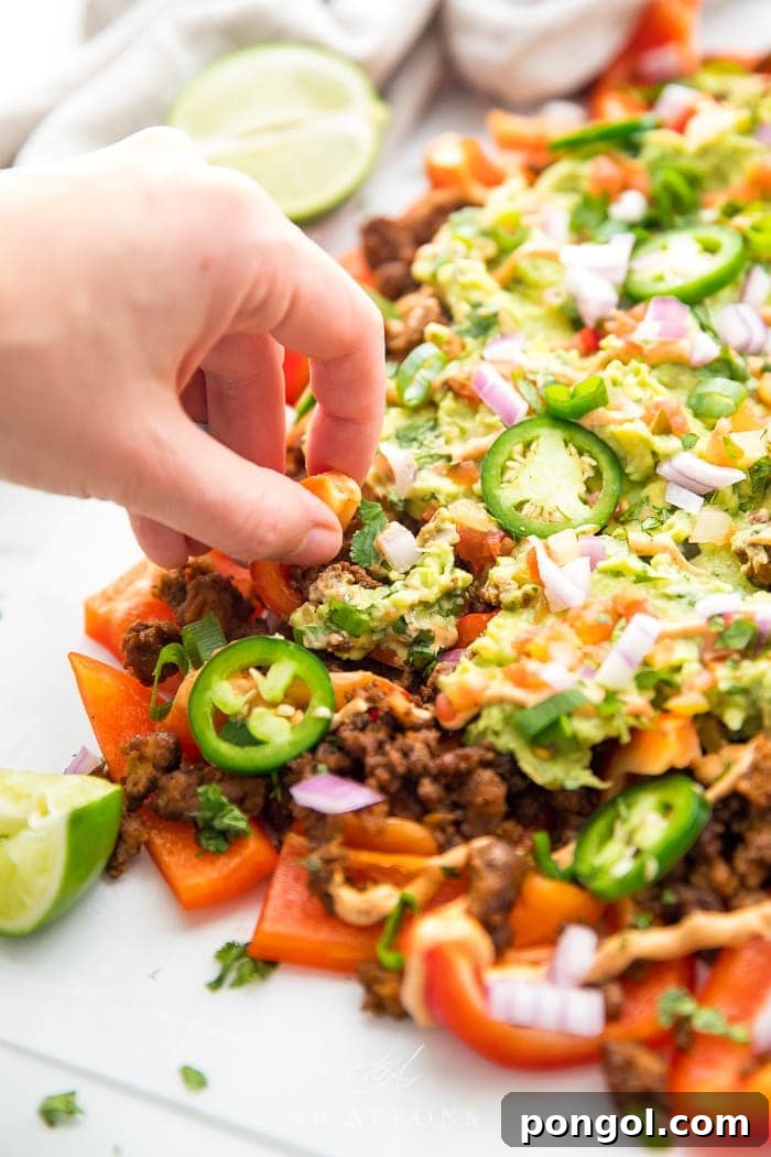 A hand reaching for a bell pepper nacho, showcasing the delicious toppings and vibrant colors