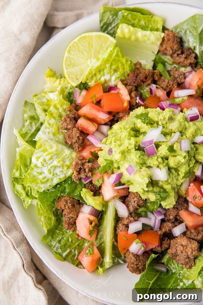 A close-up of a healthy taco salad, generously topped with guacamole, seasoned ground beef, and vibrant red onions.