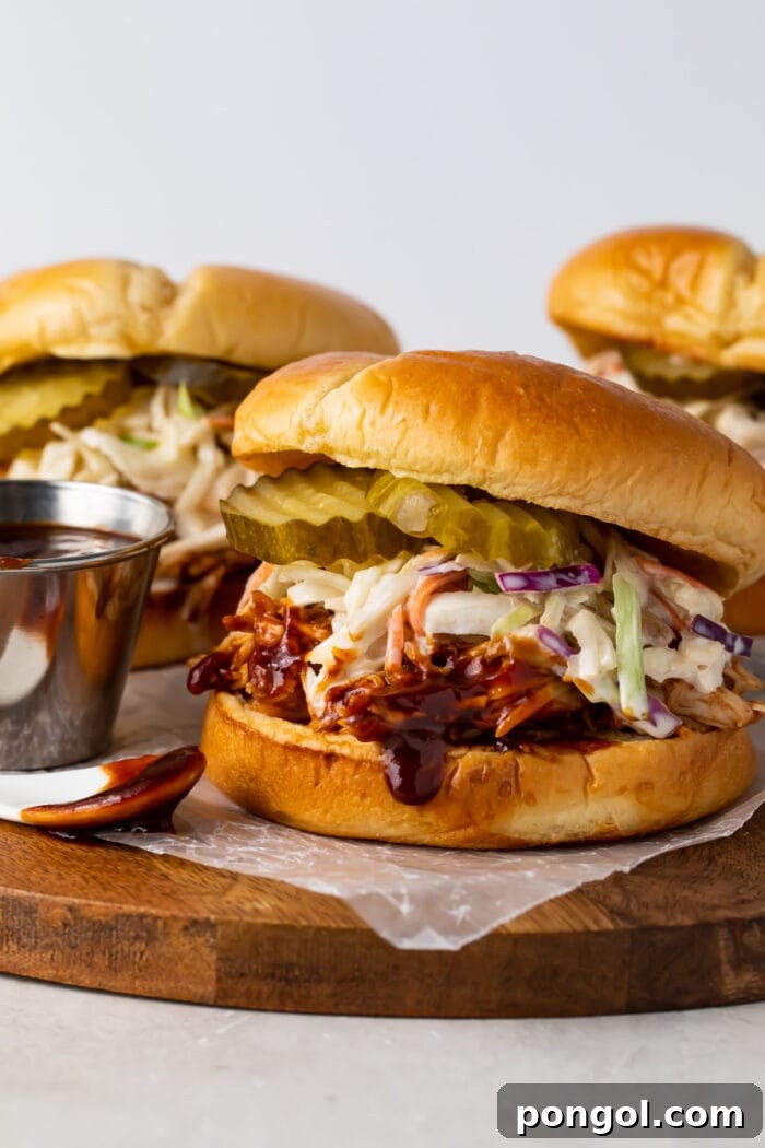 Three Instant Pot BBQ chicken sandwiches wit coleslaw and pickles