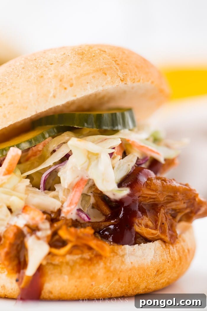 Instant Pot pulled pork served on a hamburger bun with pickles, coleslaw, and barbecue sauce.