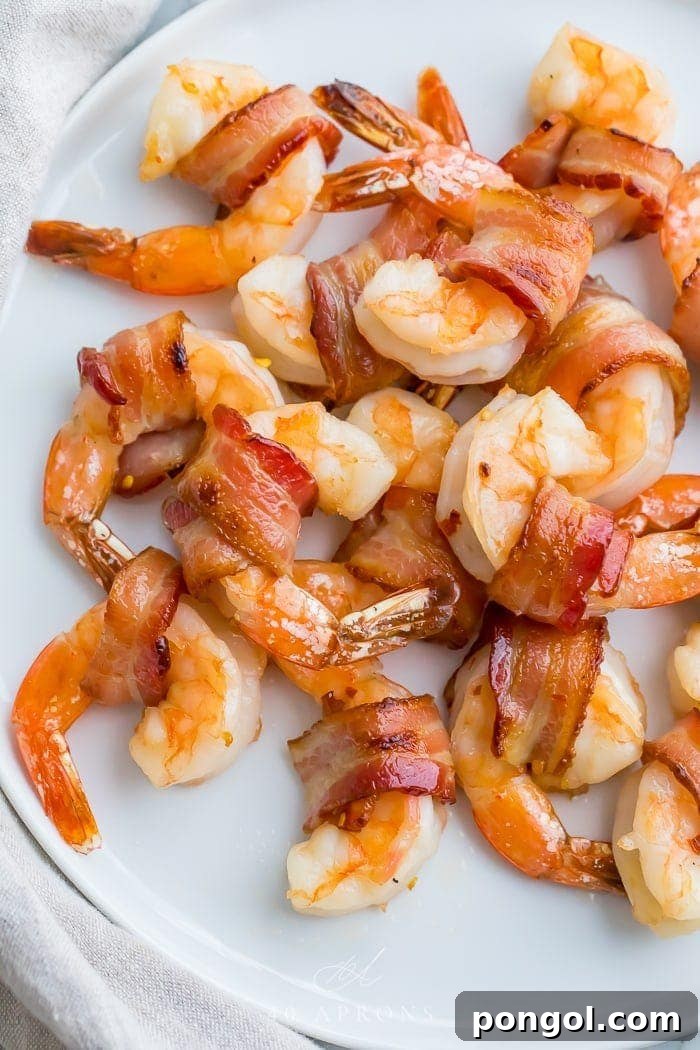 Crispy Bacon Shrimp Bites 2 Bacon wrapped shrimp on a white plate, garnished with fresh herbs