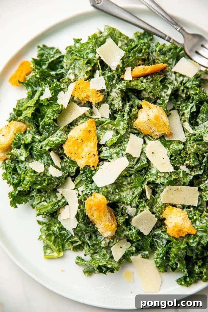 Vibrant Kale Caesar Salad on a white plate, generously topped with golden croutons and delicate parmesan shavings, ready to be enjoyed.