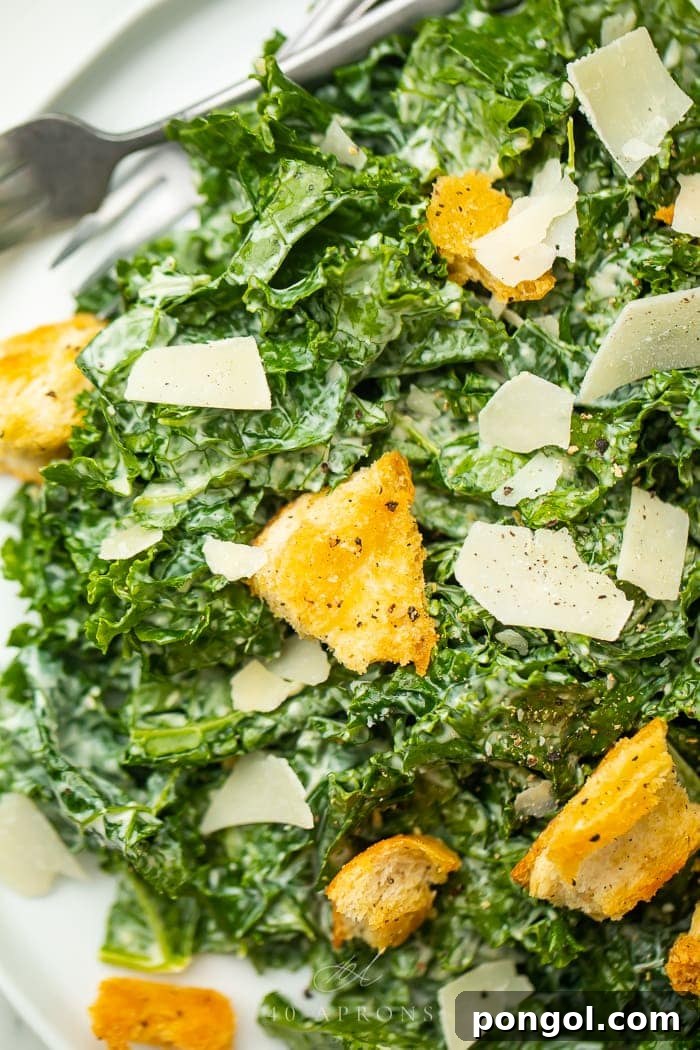Close-up view of a perfectly dressed Kale Caesar Salad, showcasing the texture of the massaged kale, golden croutons, and fine parmesan shavings.