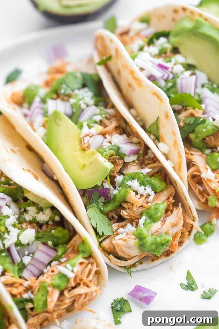 A close-up shot of Crockpot Chicken Tacos piled high with fresh toppings and a creamy avocado-cilantro sauce, showcasing their vibrant and appetizing appeal.