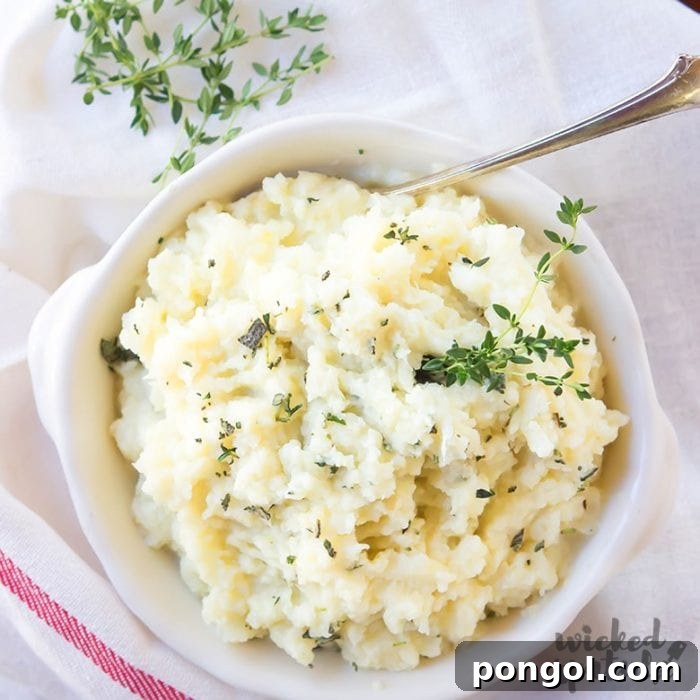 A clean white bowl filled with creamy Slow Cooker Cauliflower Mash, garnished with fresh green herbs, presenting a healthy and appetizing side dish.