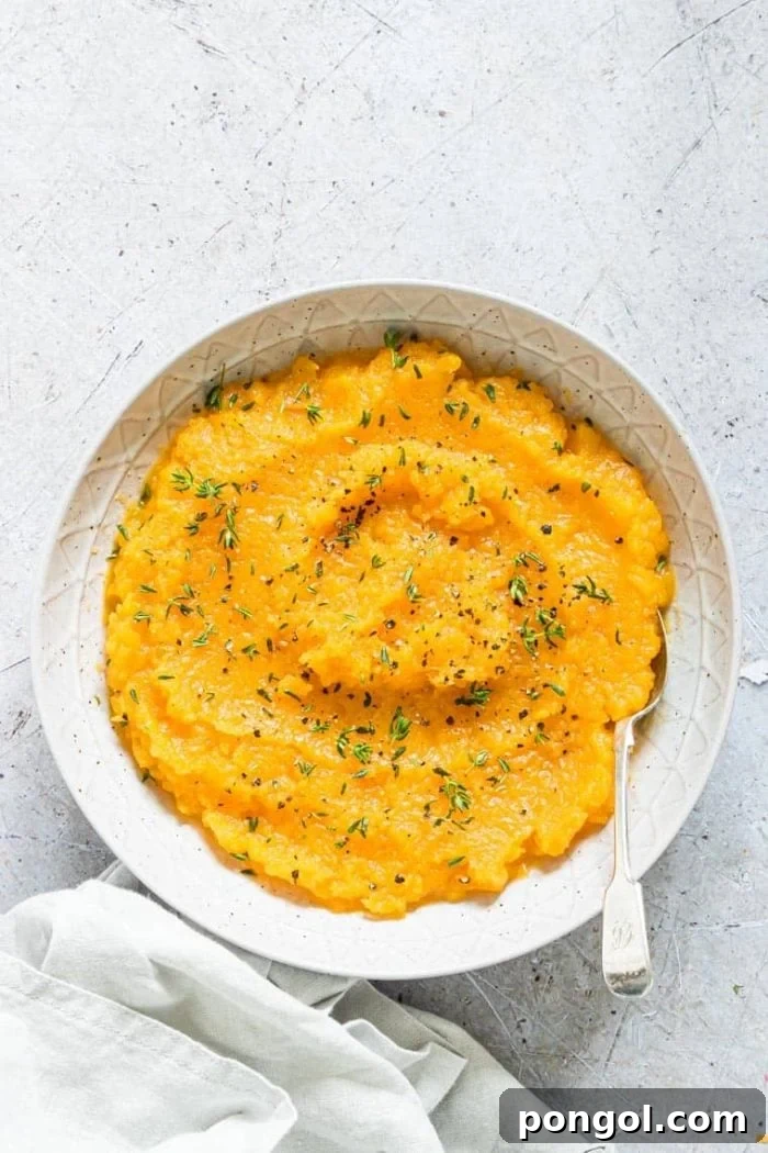 A rustic white bowl overflowing with creamy Healthier Crockpot Mashed Butternut Squash, garnished with fresh sage, inviting warmth and flavor.
