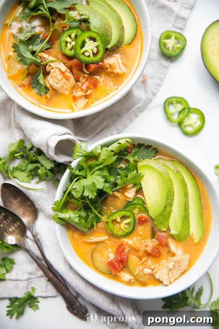 Two white bowls brimming with Whole30 Instant Pot Chicken Tortilla-Less Soup, generously garnished with sliced avocado, fresh cilantro, and vibrant jalapeños, highlighting its fresh and flavorful appeal.