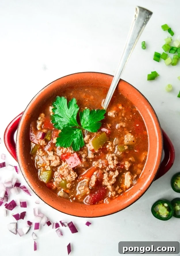 A serving of Crockpot Whole30 Chili in a white bowl, elegantly garnished with fresh green herbs, highlighting its rich texture and appetizing appearance.