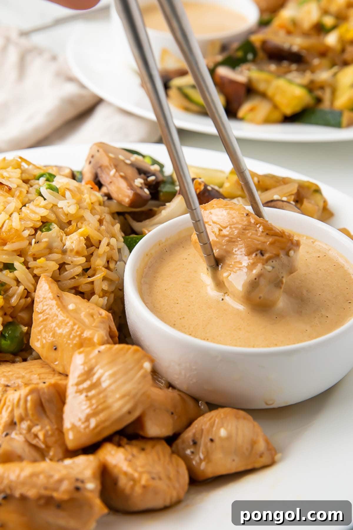 Sizzling Hibachi Chicken Dinner 2 A piece of hibachi chicken being dipped into a creamy mustard sauce on a plate with hibachi fried rice and veggies, showcasing a restaurant-quality meal at home.