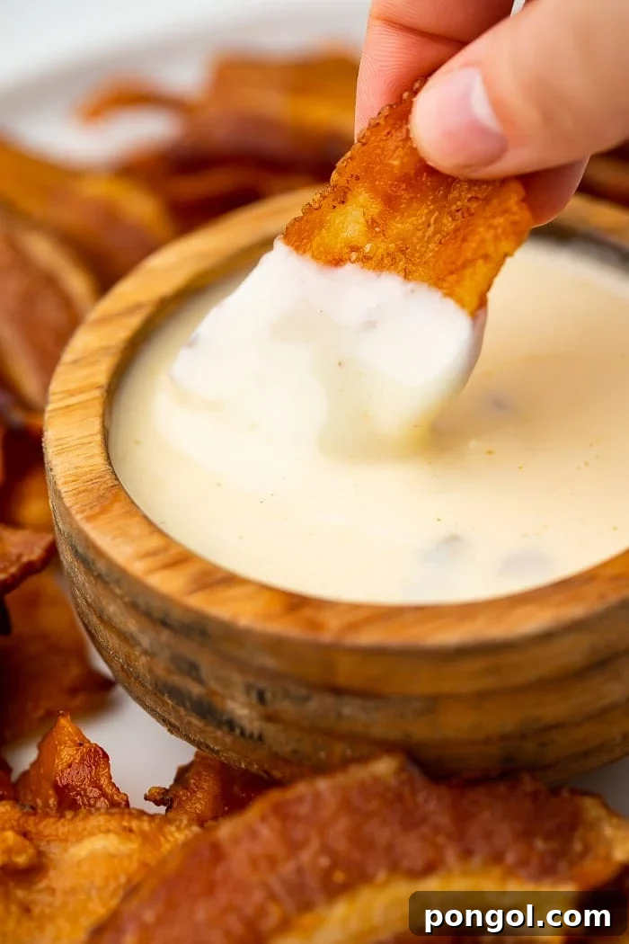 Keto Bacon Crunch 5 Close-up image of perfectly crispy bacon chips being dipped into a rich, creamy cheese dip.