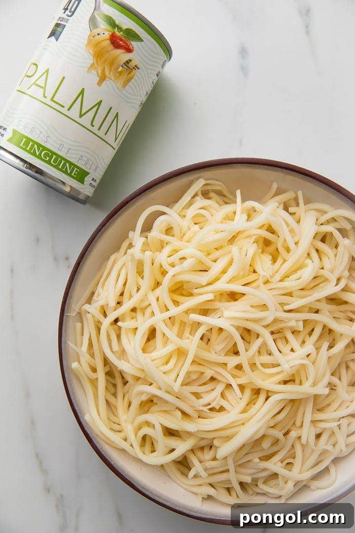 A vibrant bowl of Palmini noodles prepared with a rich sauce, positioned next to an unopened can of Palmini, illustrating its origin and prepared form.