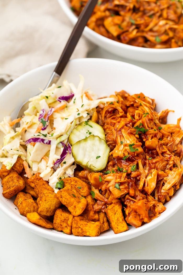 Close-up of a loaded BBQ jackfruit bowl, showing the vibrant colors of sweet potatoes, jackfruit, coleslaw, and pickles