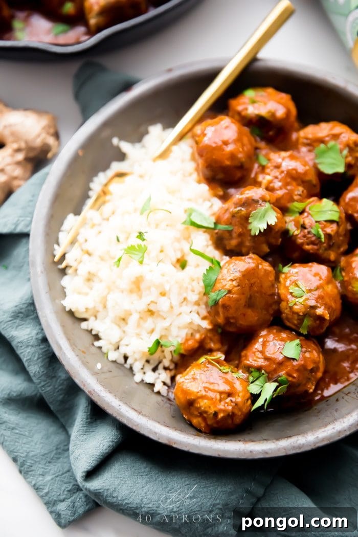 Flavorful Whole30 Dinner Ideas 49 Indian meatballs with creamy sauce served alongside cauliflower rice topped with cilantro in a grey dish on a green napkin.
