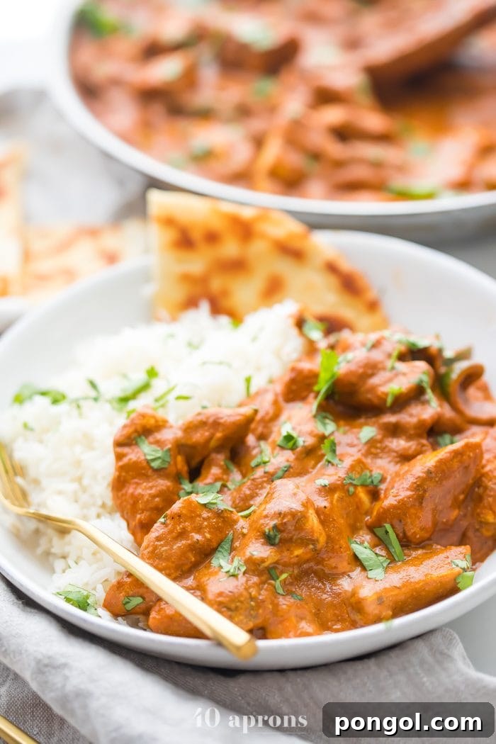 Flavorful Whole30 Dinner Ideas 5 A white bowl filled with best chicken tikka masala recipe served over rice with a side of naan, with a skillet blurred in the background.