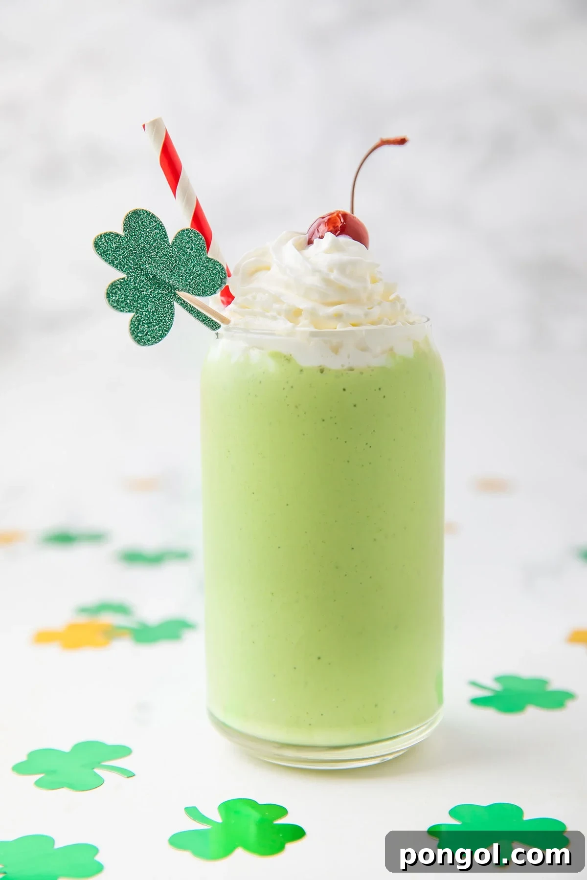 Emerald Vegan Mint Shake 2 A vibrant green dairy-free shamrock shake copycat in a tall glass, garnished with fluffy whipped cream, a maraschino cherry, and a sparkling four-leaf clover decoration.