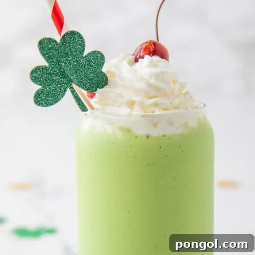Emerald Vegan Mint Shake 5 A green dairy-free shamrock shake copycat in a glass topped with whipped cream, a cherry, and a glittery four-leaf clover decoration.