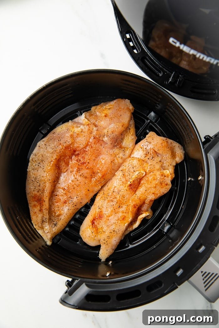 Chicken breasts actively cooking inside an air fryer basket, showing even browning