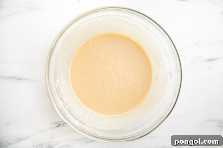 Buttermilk added to pancake batter ingredients in large glass mixing bowl, illustrating the final mixing step.