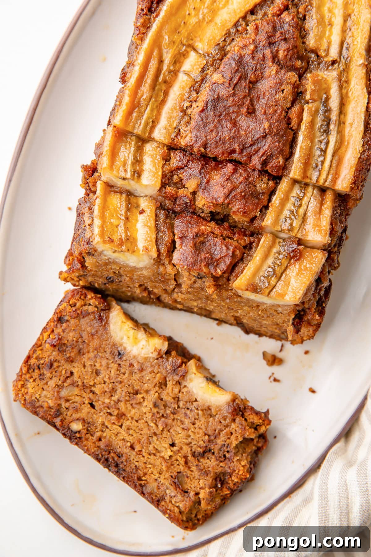A beautifully baked almond flour banana bread loaf on a serving platter, with a thick end slice resting beside it.