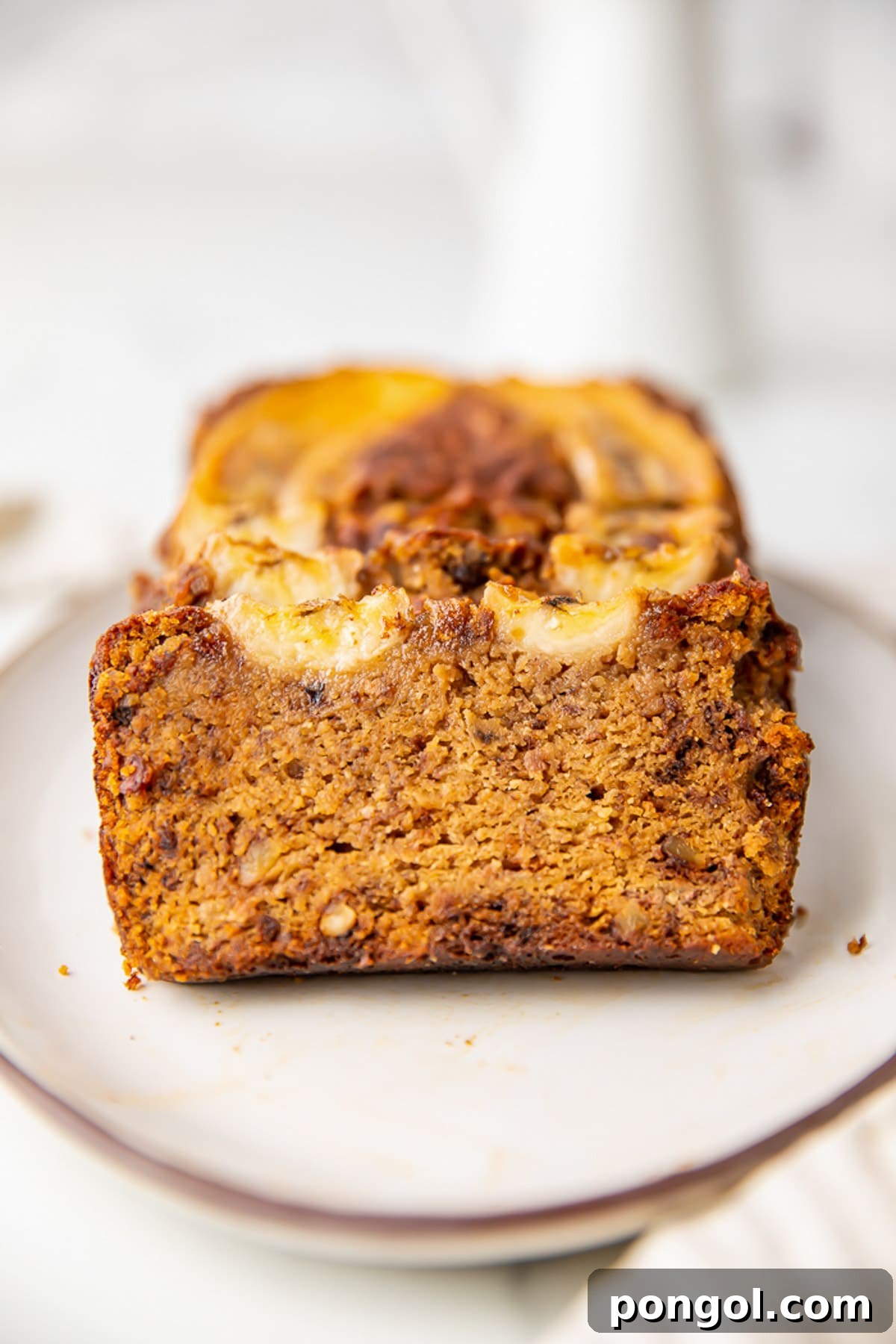 A healthy paleo almond flour banana bread loaf on a platter, with a slice removed to reveal its moist, soft interior.