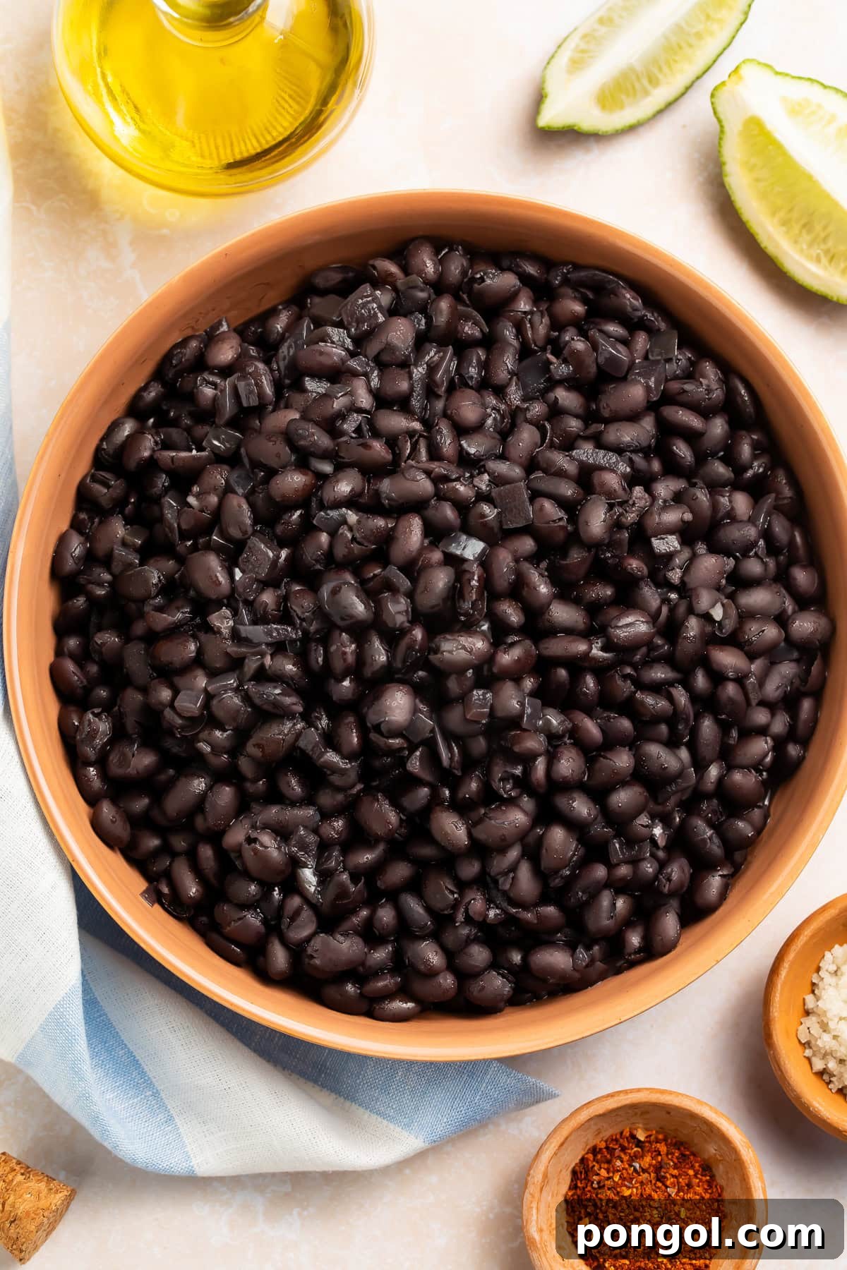 Cooked black beans in a terracotta bowl, garnished with fresh lime wedges and a drizzle of olive oil.