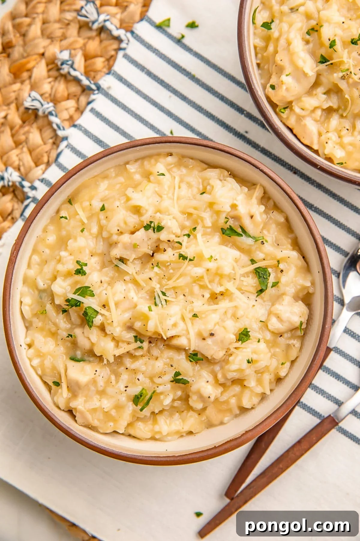 A bowl of creamy Instant Pot chicken and rice sitting on a blue and natural kitchen towel and rattan placemat, garnished with fresh herbs and a sprinkle of Parmesan.