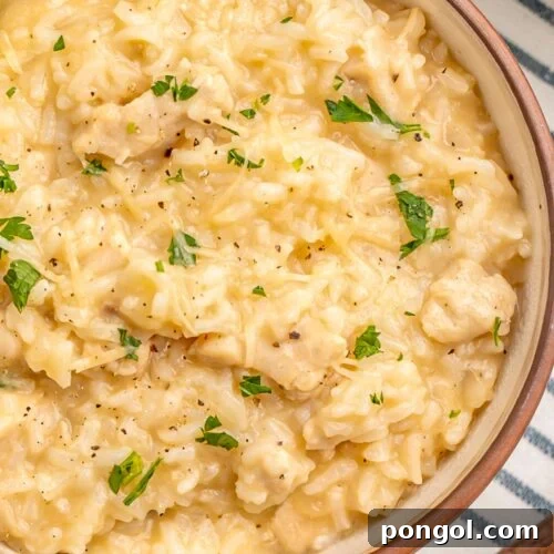 Bowl of creamy Instant Pot chicken and rice with melted Parmesan cheese and fresh parsley on a striped kitchen towel.