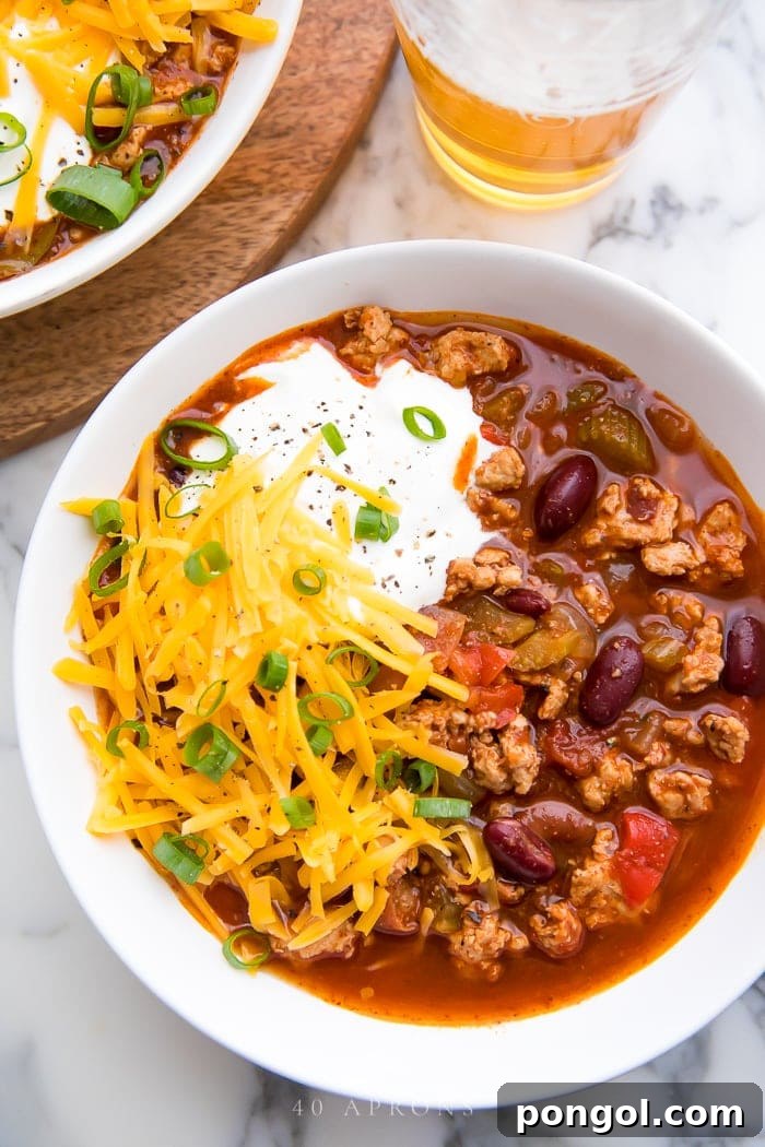 A top-down shot of slow cooker turkey chili, served in a rustic bowl with fresh toppings like shredded cheese, green onions, and sour cream, perfect for a cozy meal.