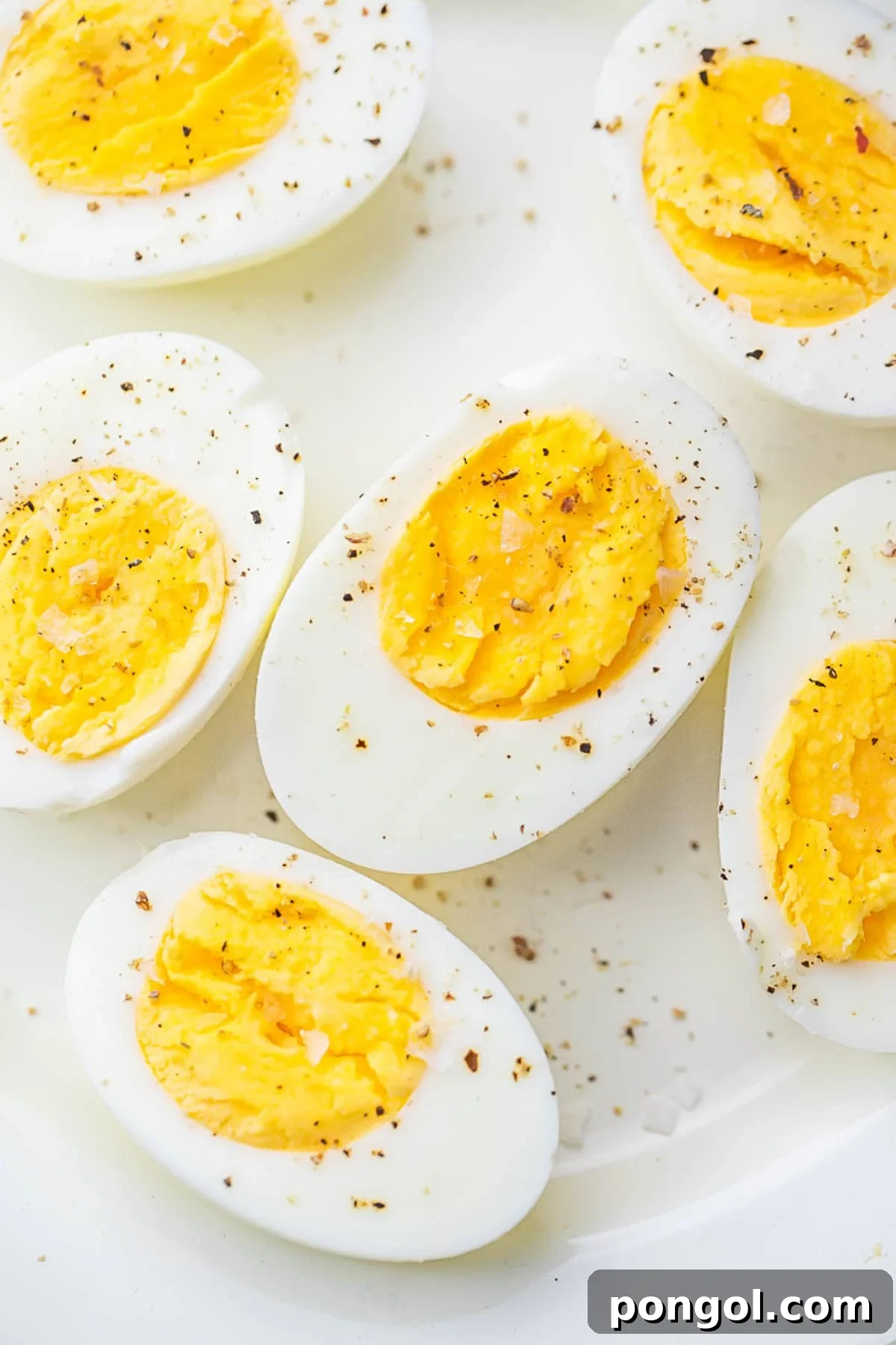 Air fryer hard-boiled eggs, cut in half and seasoned with black pepper, resting on a plate.