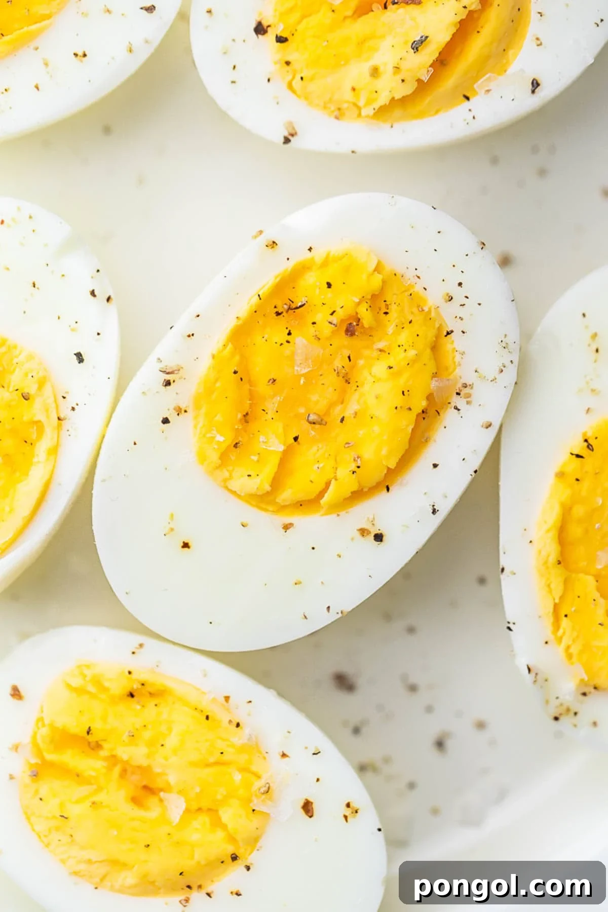 Air fryer hard-boiled eggs, cut in half and seasoned with black pepper, resting on a plate.