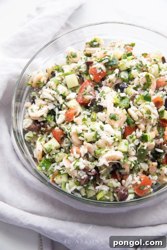 A refreshing Greek shrimp salad, featuring succulent shrimp, crumbled feta cheese, and fluffy rice, tossed with fresh vegetables and herbs.