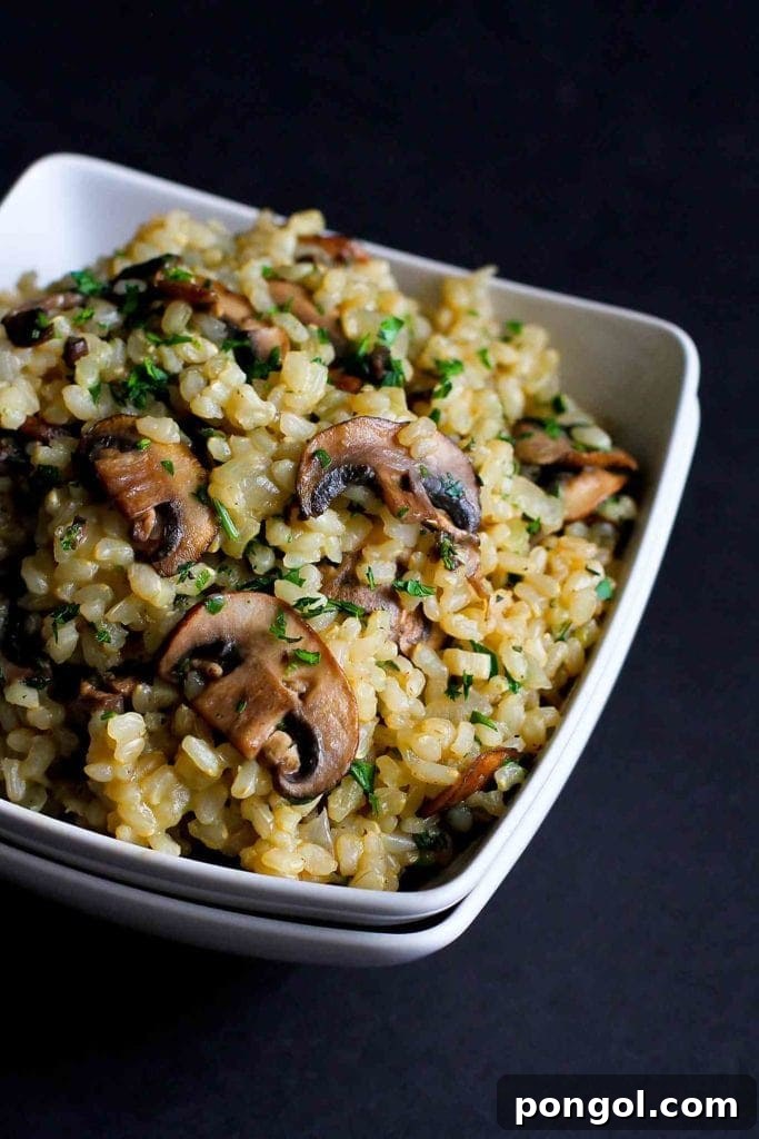 A close-up of toasted brown rice with mushrooms and thyme, highlighting the earthy textures and aromatic seasoning of this side dish.