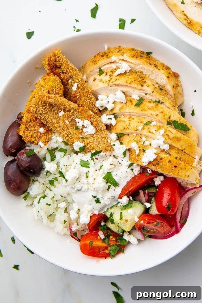 A vibrant and generously portioned Greek chicken bowl, brimming with lemony rice, seasoned chicken, fresh vegetables, and creamy tzatziki.