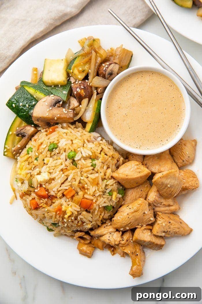 A plate featuring authentic hibachi chicken, perfectly fried rice, and crisp sautéed vegetables, reminiscent of a Japanese steakhouse experience.