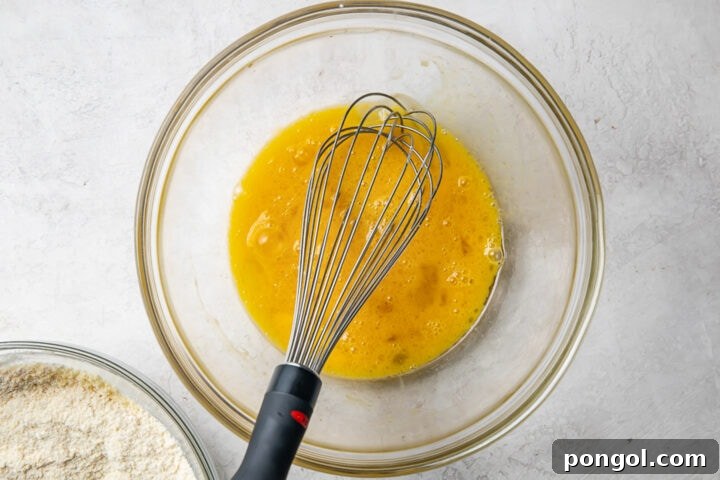 Wet ingredients for paleo pancakes in a large glass mixing bowl with a whisk.
