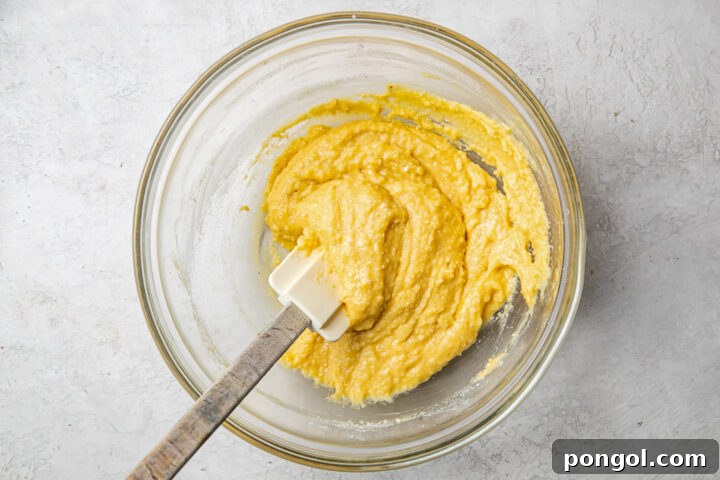 Wet and dry ingredients for paleo pancakes in a glass mixing bowl with a silicone spatula.