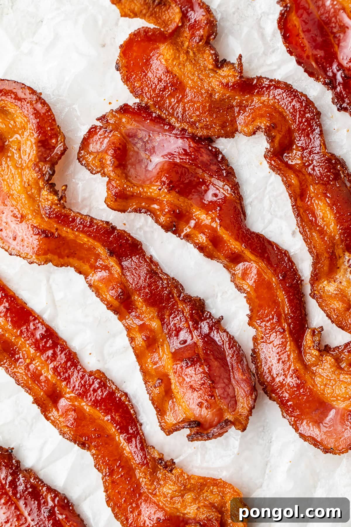 Crispy Air Fryer Bacon 2 Air fryer bacon strips placed on a sheet of parchment paper, positioned at an angle, highlighting their perfect crispiness.